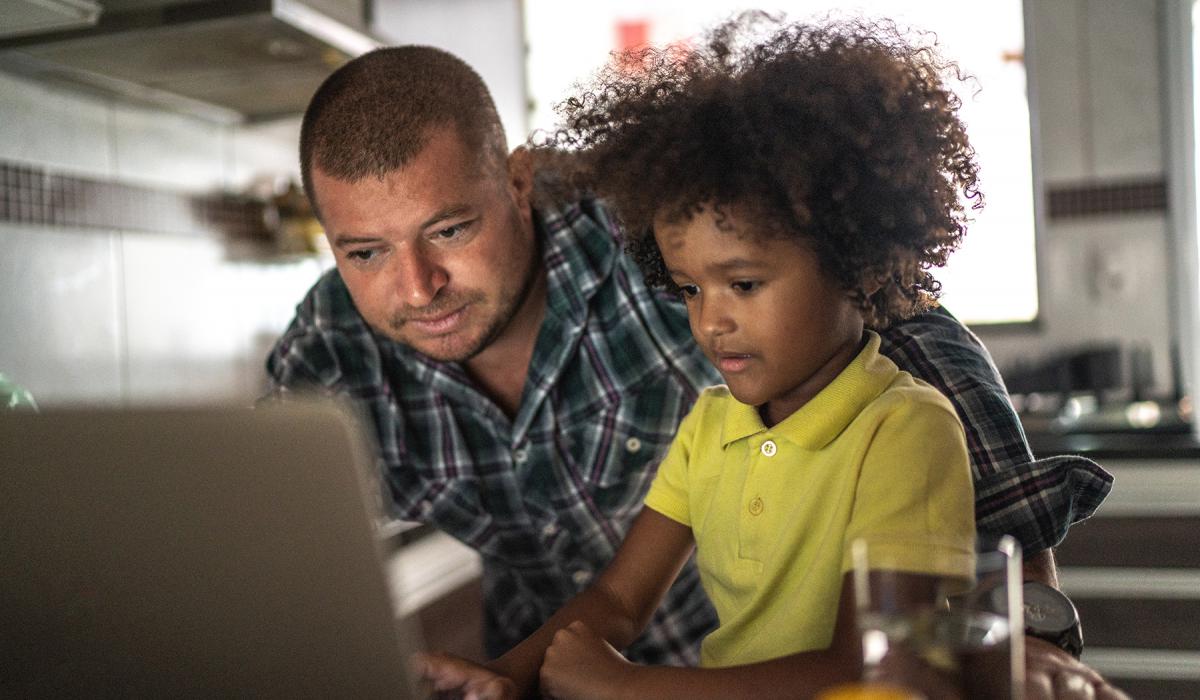 Man and elementary-school boy working together at laptop indoors.